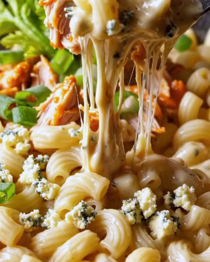 A close-up of a steaming bowl of buffalo pulled chicken mac and cheese topped with gorgonzola and fresh herbs.