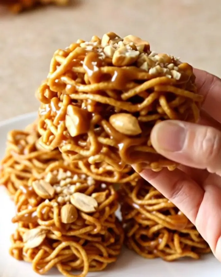 A close-up of golden, crunchy butterscotch haystacks piled on a white plate with a soft-focus kitchen background.
