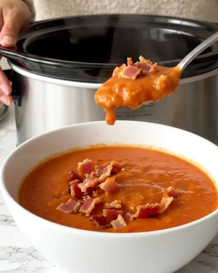 A bowl of creamy tomato soup topped with crispy bacon bits, served in a white shallow bowl.