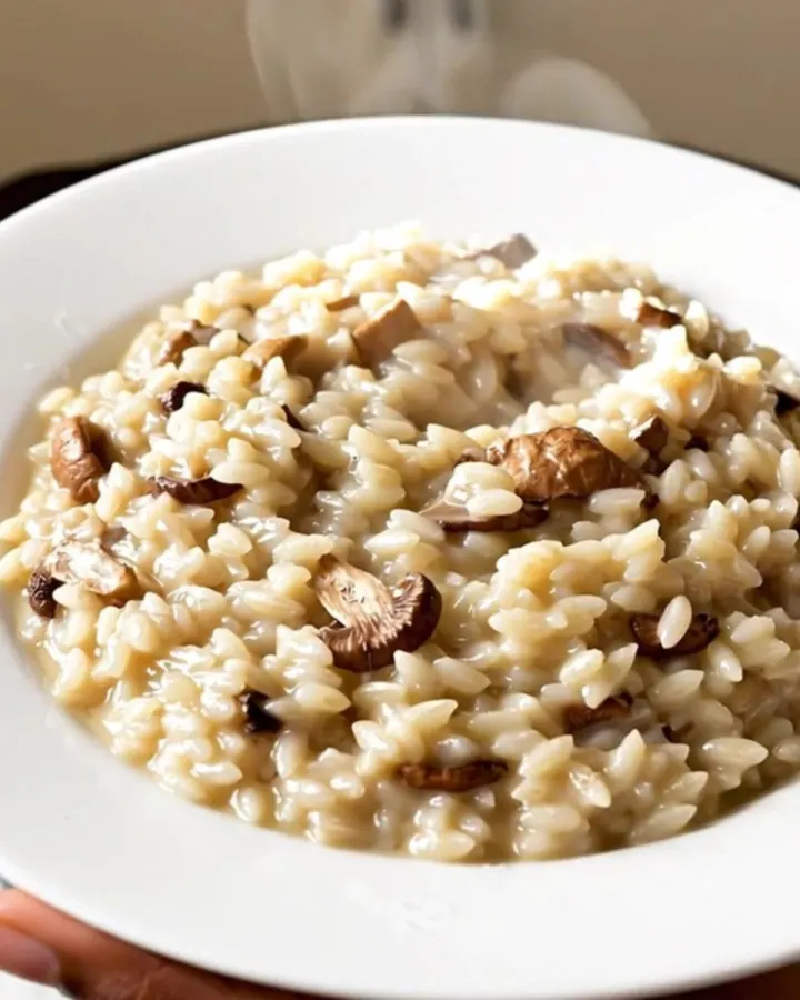 A top-down view of creamy porcini mushroom risotto in a white bowl, showing a glossy and steaming texture.