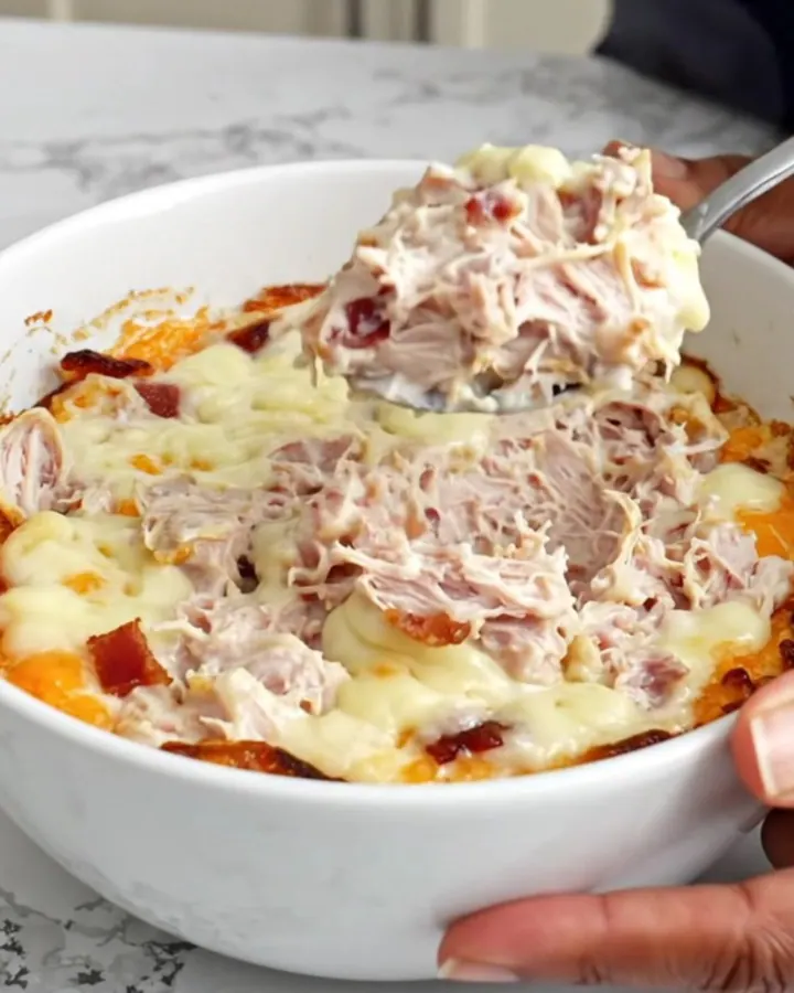 A top-down view of a slow cooker filled with creamy turkey and bacon dip, featuring melted cheese and visible chunks of meat.
