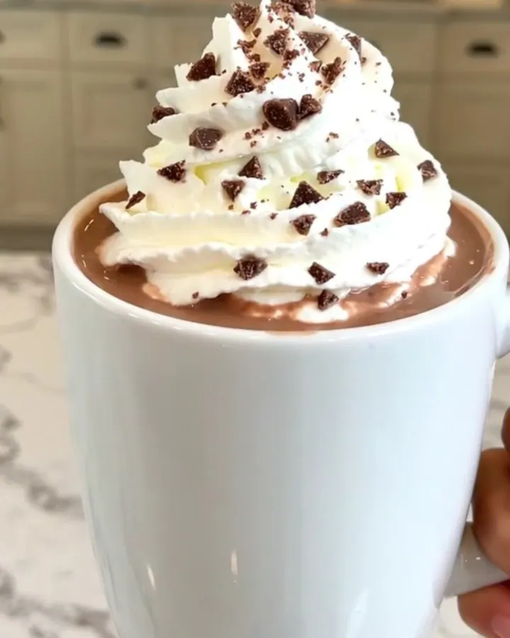 A steaming mug of peppermint hot chocolate topped with whipped cream on a table.