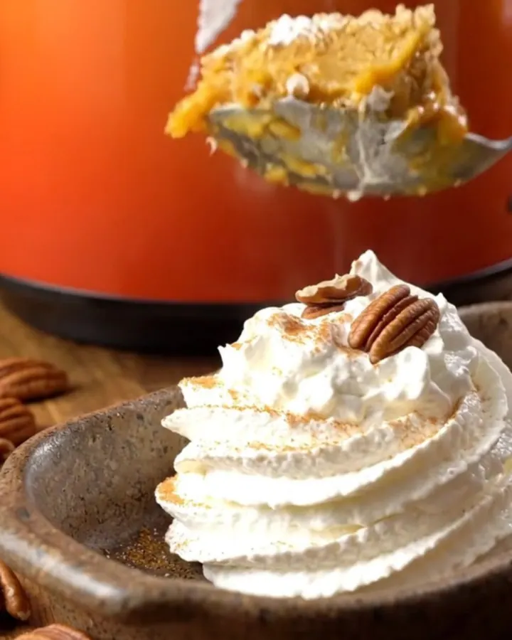 A warm, golden pumpkin pecan crunch cake served in a stoneware dish with whipped cream.