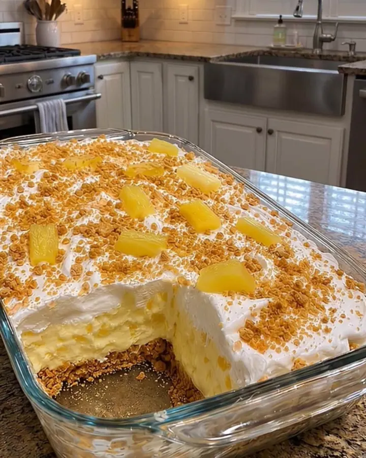 Dessert crémeux à l’ananas sans four dans un plat en verre, un carré levé à la spatule montrant la base sablée