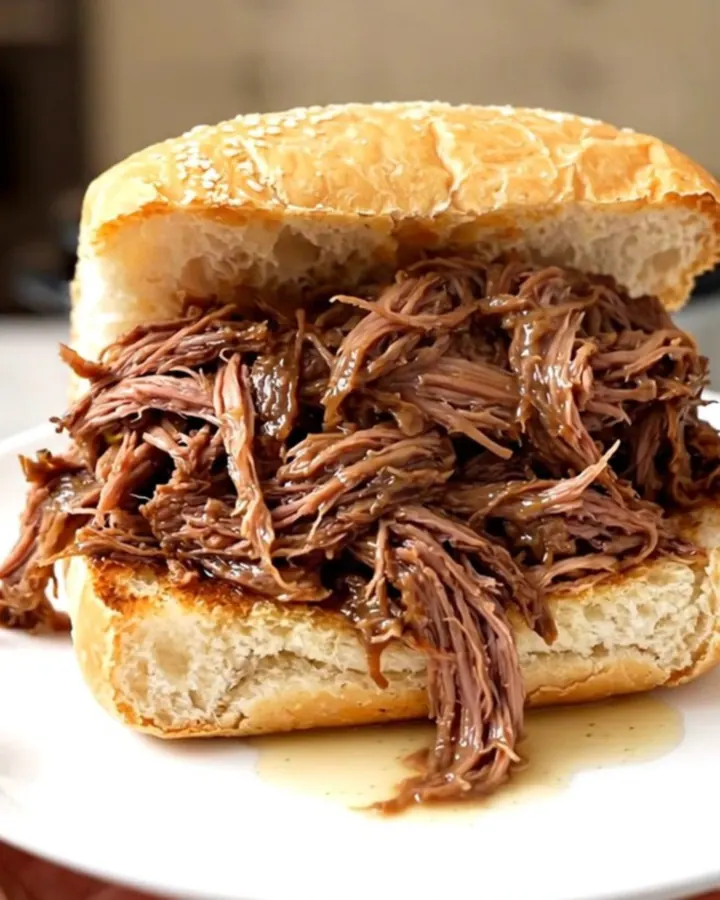 A steaming, juicy Italian beef sandwich on a crusty roll held on a white plate.
