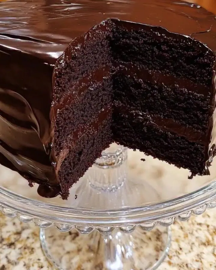 Gâteau au chocolat noir en trois couches au glaçage soyeux, une part coupée posée sur un présentoir en verre