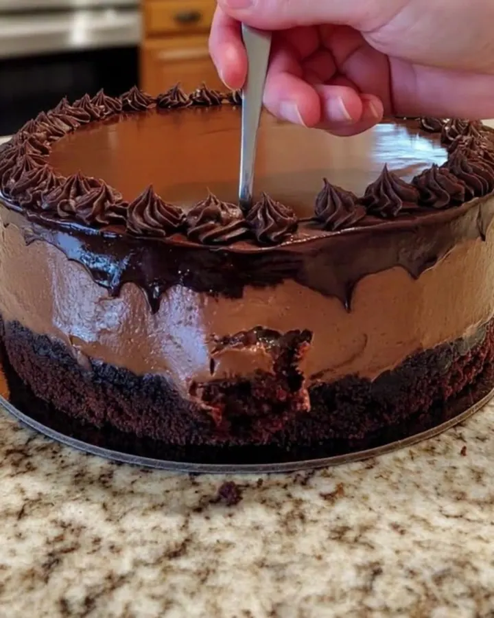 Gâteau mousse au chocolat entier sur un plan de travail, ganache brillante et rosettes pochetées en bordure