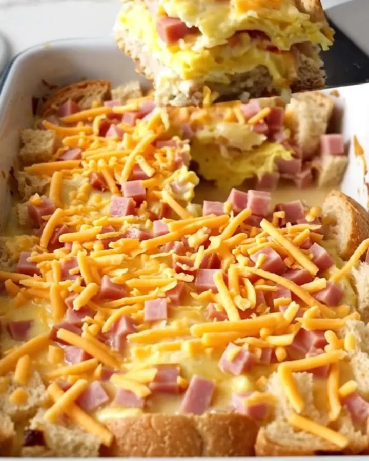 A golden-brown ham and cheddar breakfast strata in a white baker on a speckled countertop.