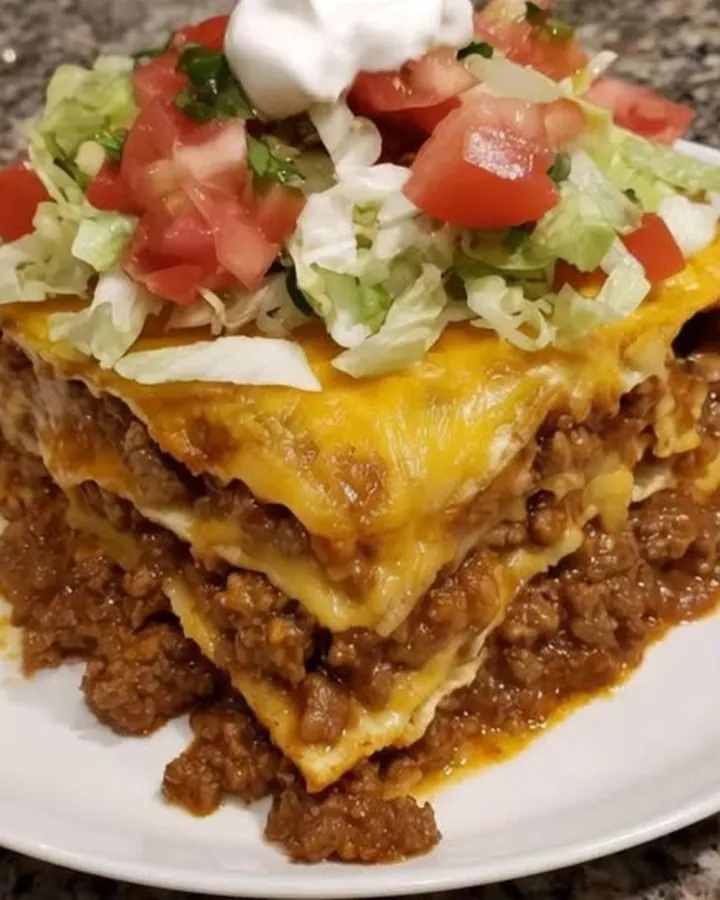 Tranche haute de lasagna de tacos sur assiette blanche, cheddar filant, laitue émincée