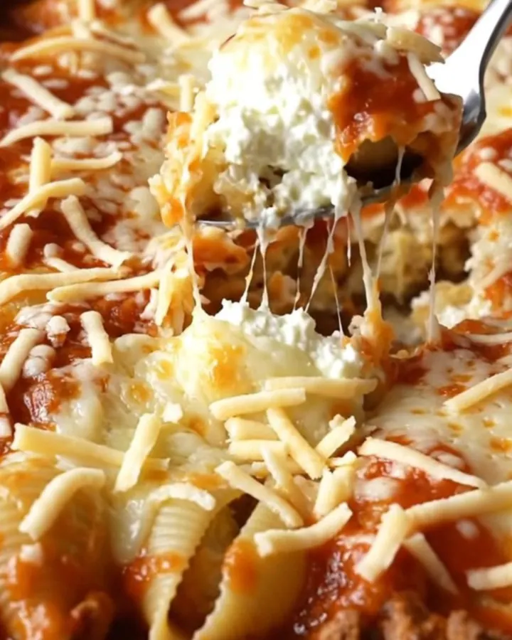 A large rectangular ceramic dish filled with unbaked pasta shells, dollops of ricotta, and marinara sauce.