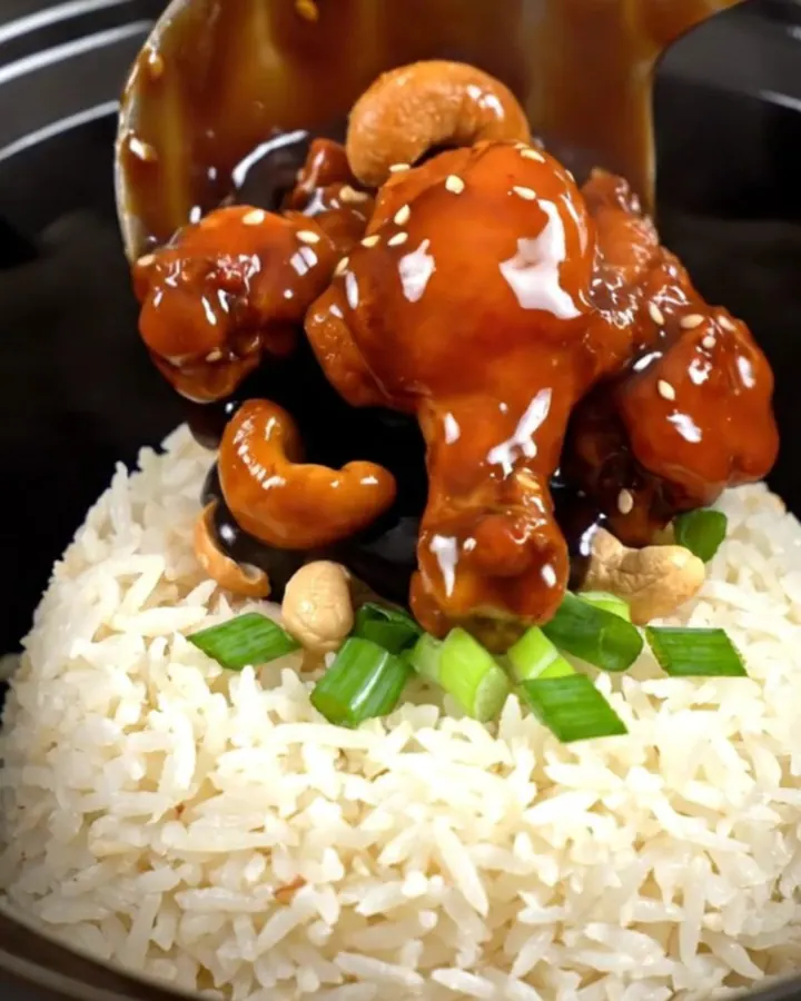 A close-up of glossy Kung Pao chicken with roasted cashews and scallions served in a bowl.