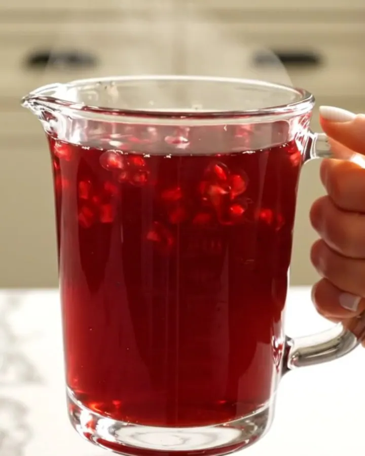 A warm glass mug filled with deep-red spiced pomegranate apple cider, garnished with a cinnamon stick.