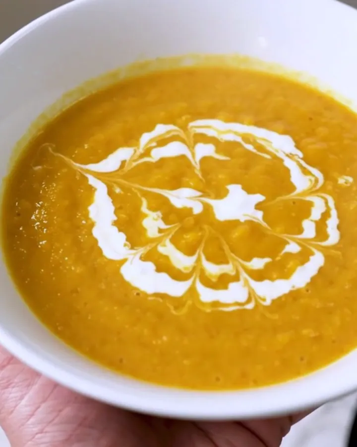 Soupe de potiron onctueuse servie dans un bol blanc avec un tourbillon de crème fraîche sur le dessus
