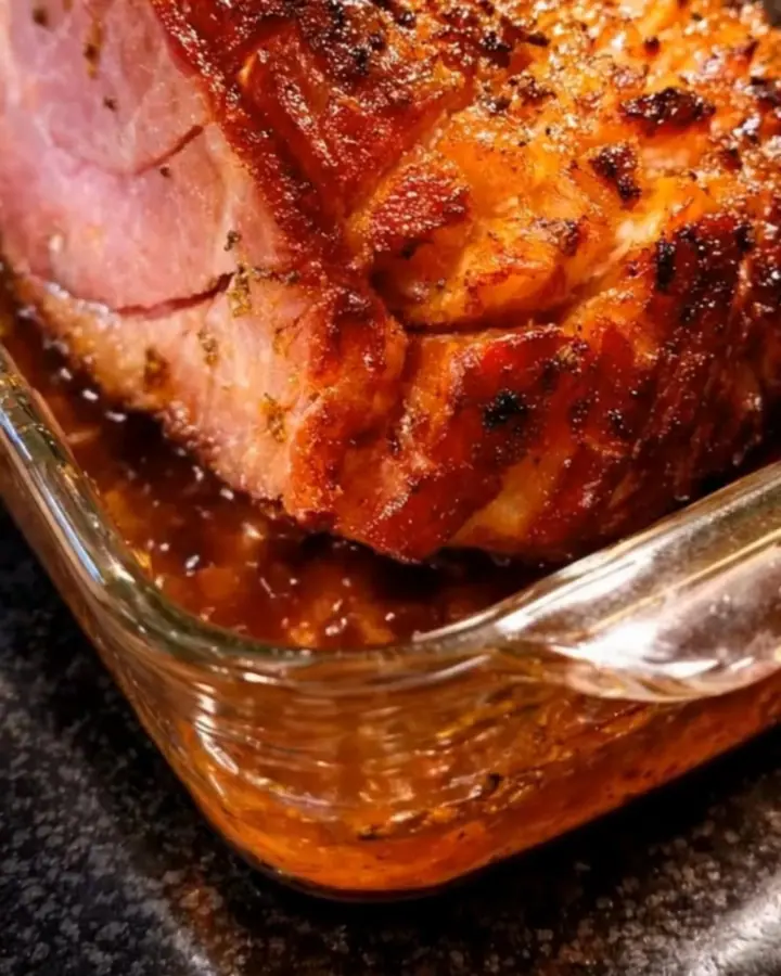 A beautifully glazed, golden-brown honey baked ham sitting in a glass dish on a rustic kitchen counter.