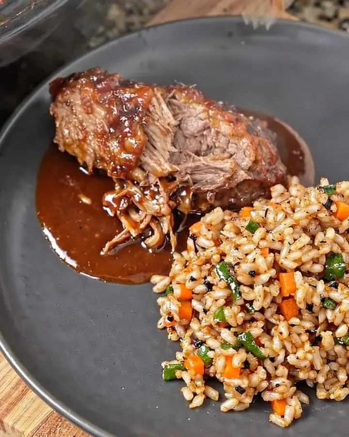 Travers de bœuf braisés fondants servis avec un riz sauté aux légumes colorés dans une assiette.