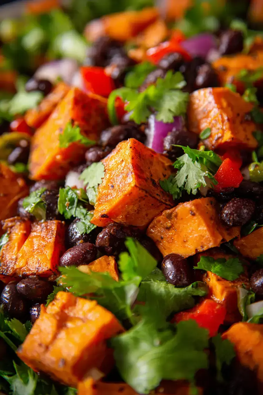 A vibrant bowl of sweet potato black bean salad served alongside grilled chicken and fresh lime wedges